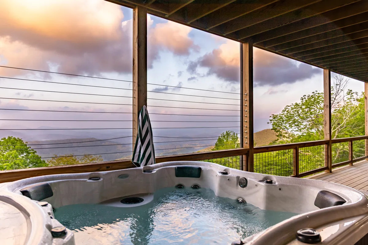A serene outdoor hot tub sits on a wooden deck, overlooking breathtaking mountain views. The scene is tranquil, with clouds drifting above and the deck railing framing the expansive vista, suggesting a perfect spot for relaxation and family gatherings after a day of activities.