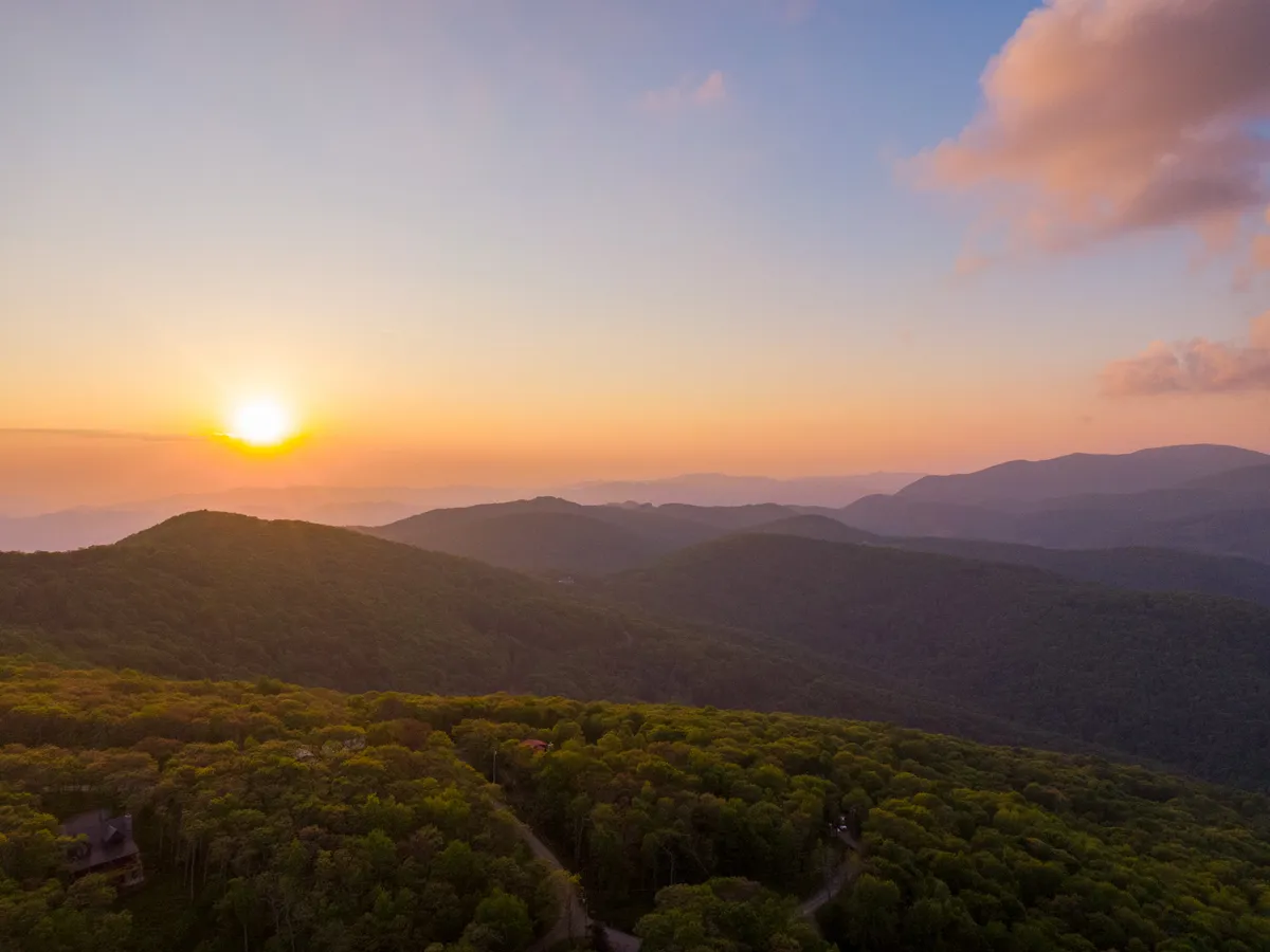 A stunning view of a sunset over a mountain range and dense forest, evoking tranquility and the adventure of the local area. The natural beauty on display invites exploration and meaningful group experiences in the surrounding region.