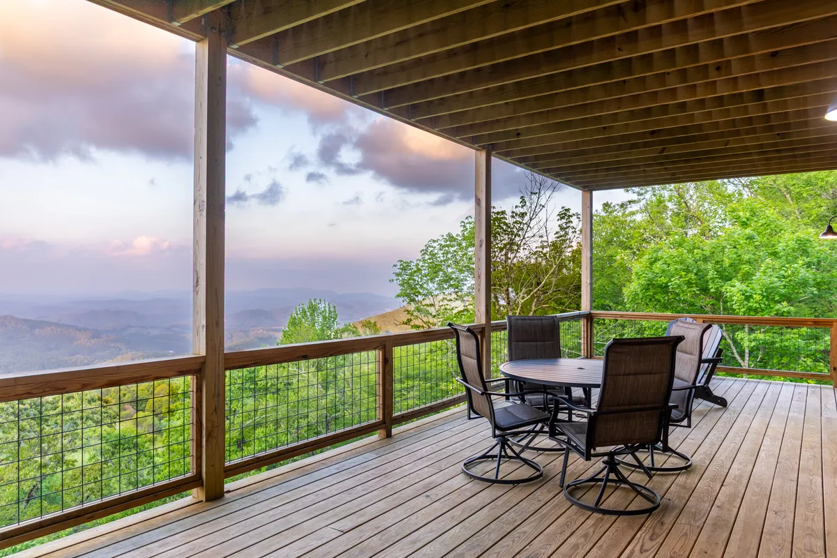 A peaceful wooden deck is furnished with comfortable outdoor seating, overlooking a vast mountain view. The scene suggests a tranquil space ideal for relaxing, sharing romantic evenings, or stargazing together. The seating arrangement encourages intimate connection, surrounded by nature's beauty.