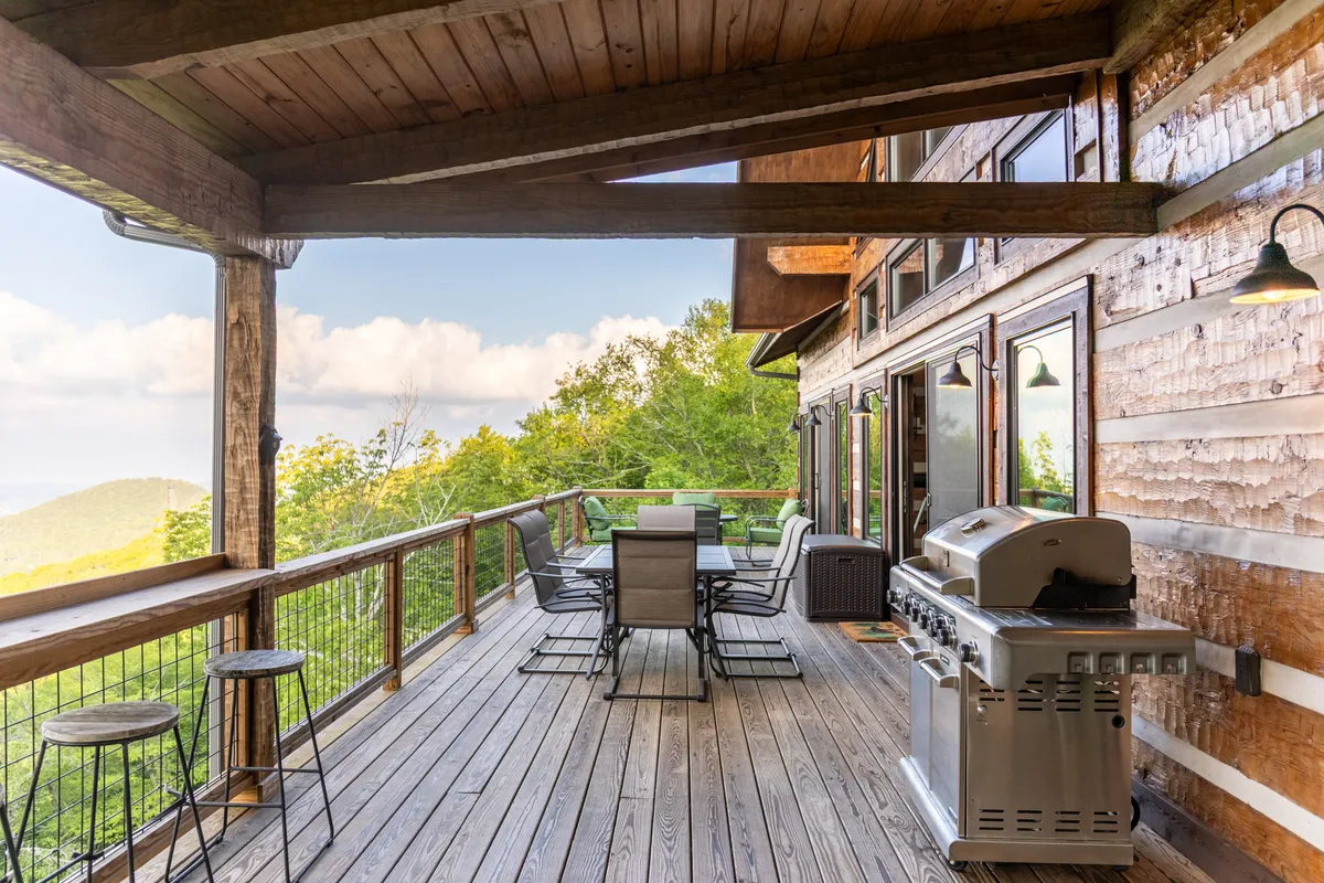 A spacious wooden deck features an outdoor dining set and grill, set against a panoramic mountain backdrop. The scene hints at al fresco dining, shared breakfasts at sunrise, or leisurely evening gatherings—activities ideal for couples seeking both privacy and connection.