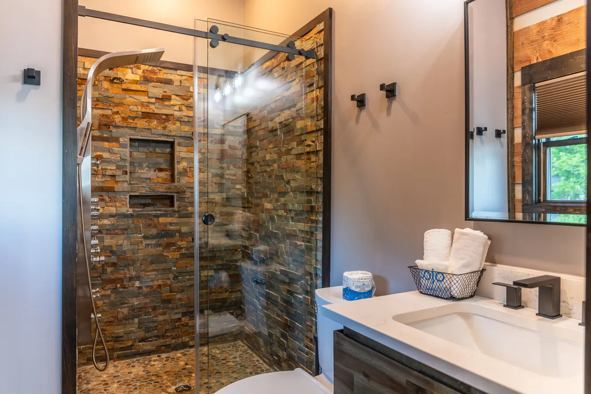 A spa-inspired bathroom with a glass-enclosed shower against a natural stone wall, modern sink and fixtures, and neatly arranged towels. The ambiance is tranquil and elevates the sense of luxury and privacy described in the content.