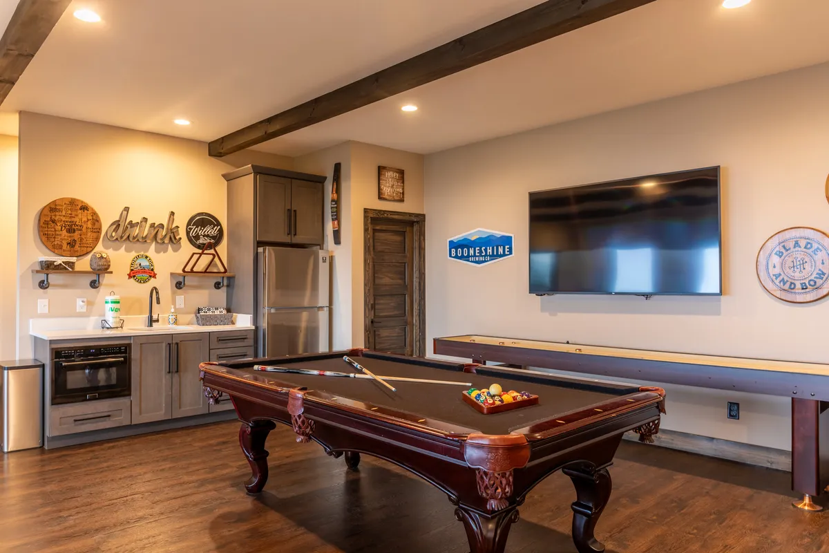 A lively game room featuring a pool table, kitchenette, and a television, with rustic barrel décor. The space is designed for casual fun and socializing, ideal for group activities like game nights or enjoying drinks together.