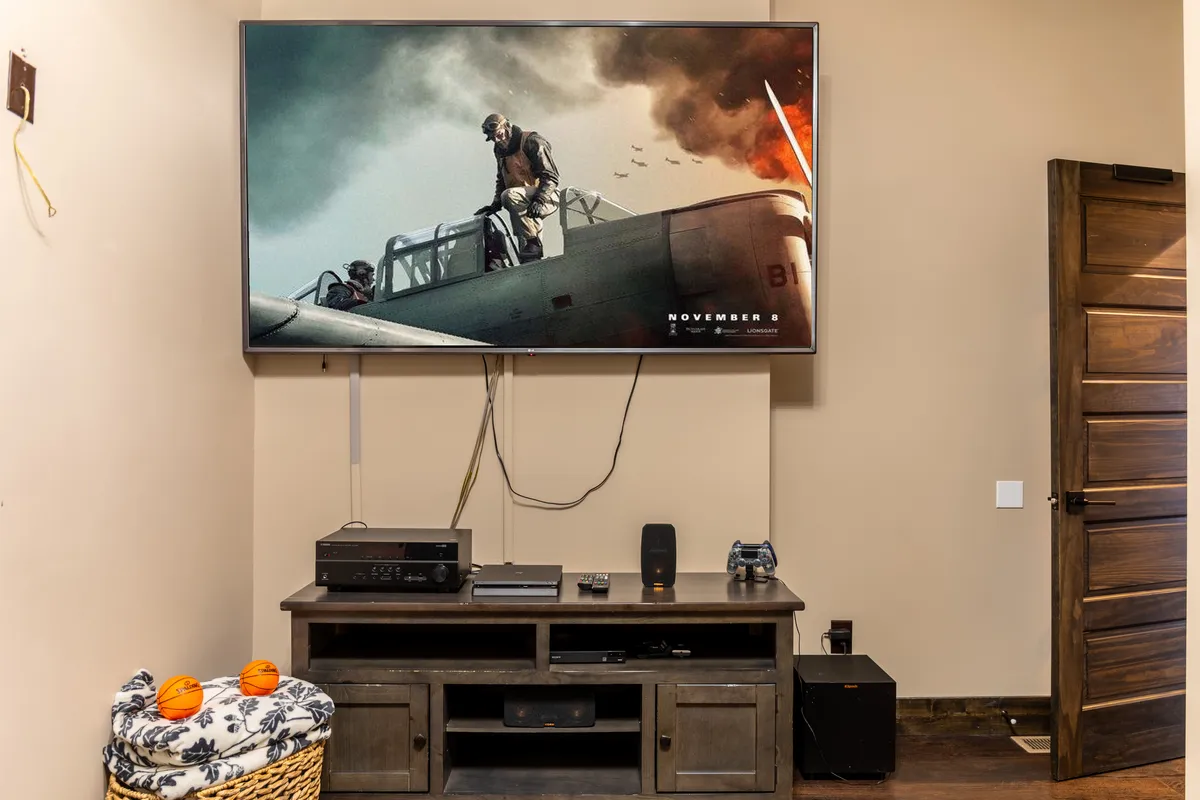 A cozy, dedicated theater room with a large TV screen displaying a movie, an entertainment console, and a basket with blankets and toys, creating the perfect setting for immersive family movie nights or video game sessions.