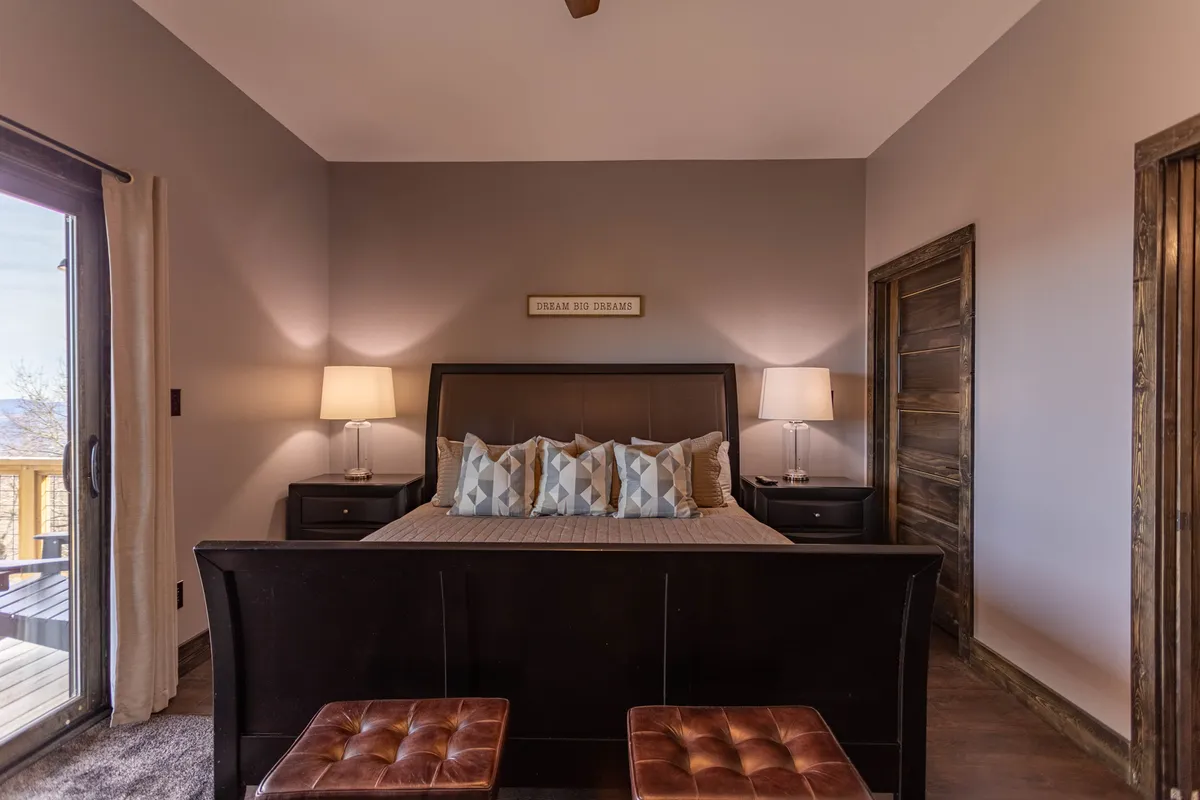 A well-lit king bedroom featuring a plush bed with decorative pillows, nightstands with lamps on each side, and a large window that fills the space with natural light. The serene atmosphere is underscored by the soothing color palette and cozy textures, creating an inviting place for rest and rejuvenation.