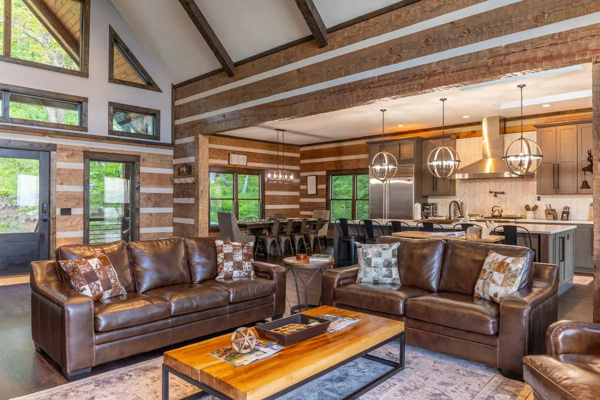 A welcoming open interior showing leather sofas, a wooden coffee table, and a clear view of the kitchen area with pendant lights and a spacious dining table. The arrangement encourages socializing, family gatherings, and shared culinary experiences.