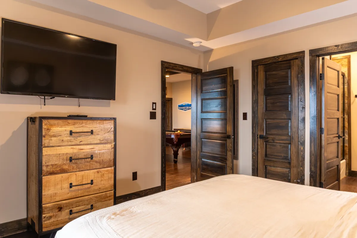 A welcoming bedroom scene featuring a wooden dresser, a flat-screen TV, and open doors leading to adjacent spaces. The setup is inviting for relaxing in bed, watching movies, or family bonding.
